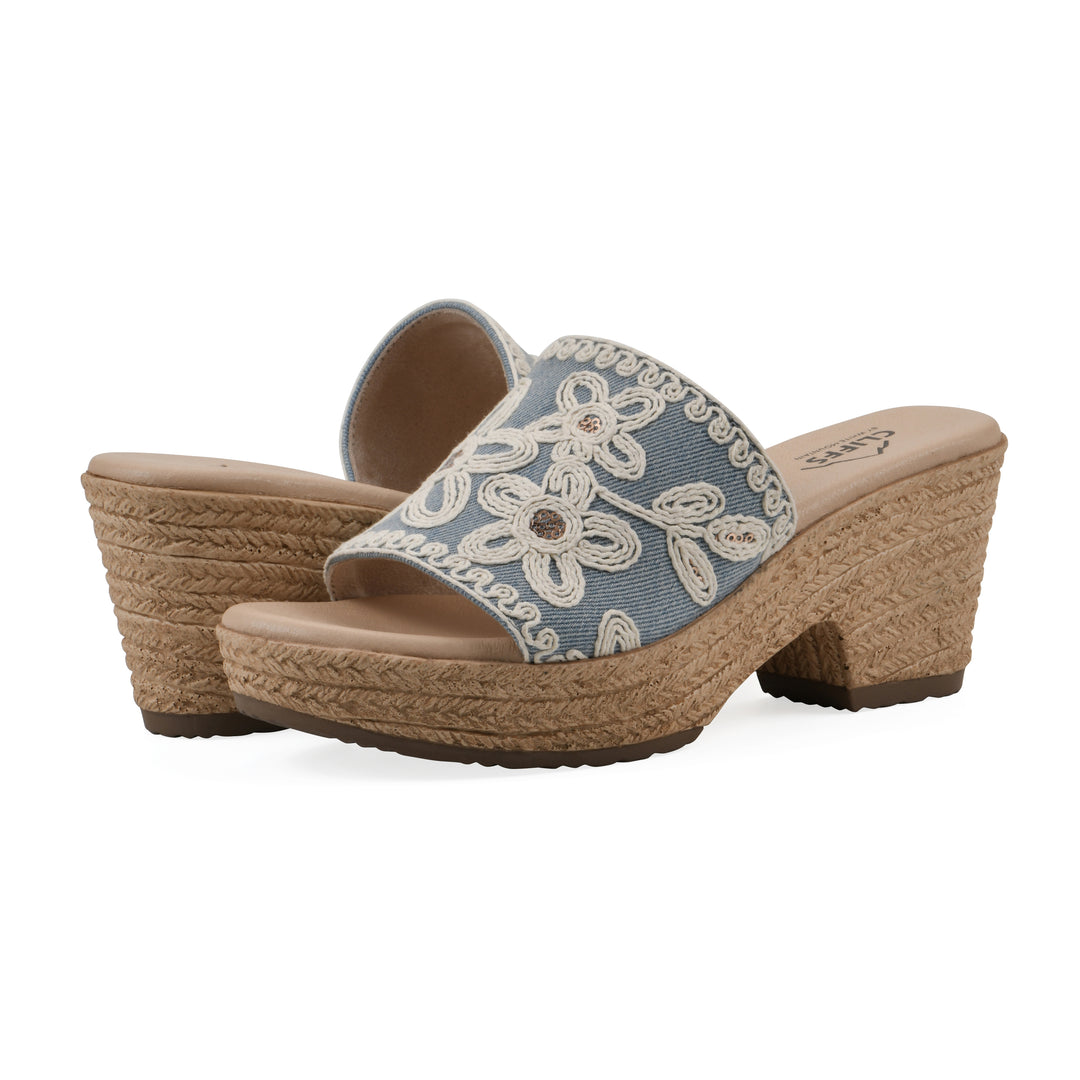 Angle view of a pair of denim wedge  sandals with cream embroidered floral pattern and a braided rope-style sole