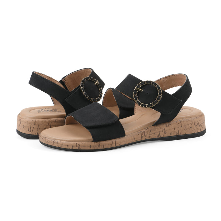 Angle view of a pair of black sandals with double adjustable straps, circular buckle embellishment, and low cork print wedge 