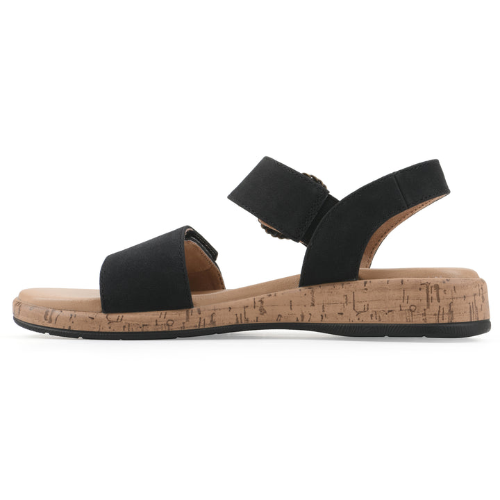 Side view of a black sandal with double adjustable straps, circular buckle embellishment, and low cork print wedge 