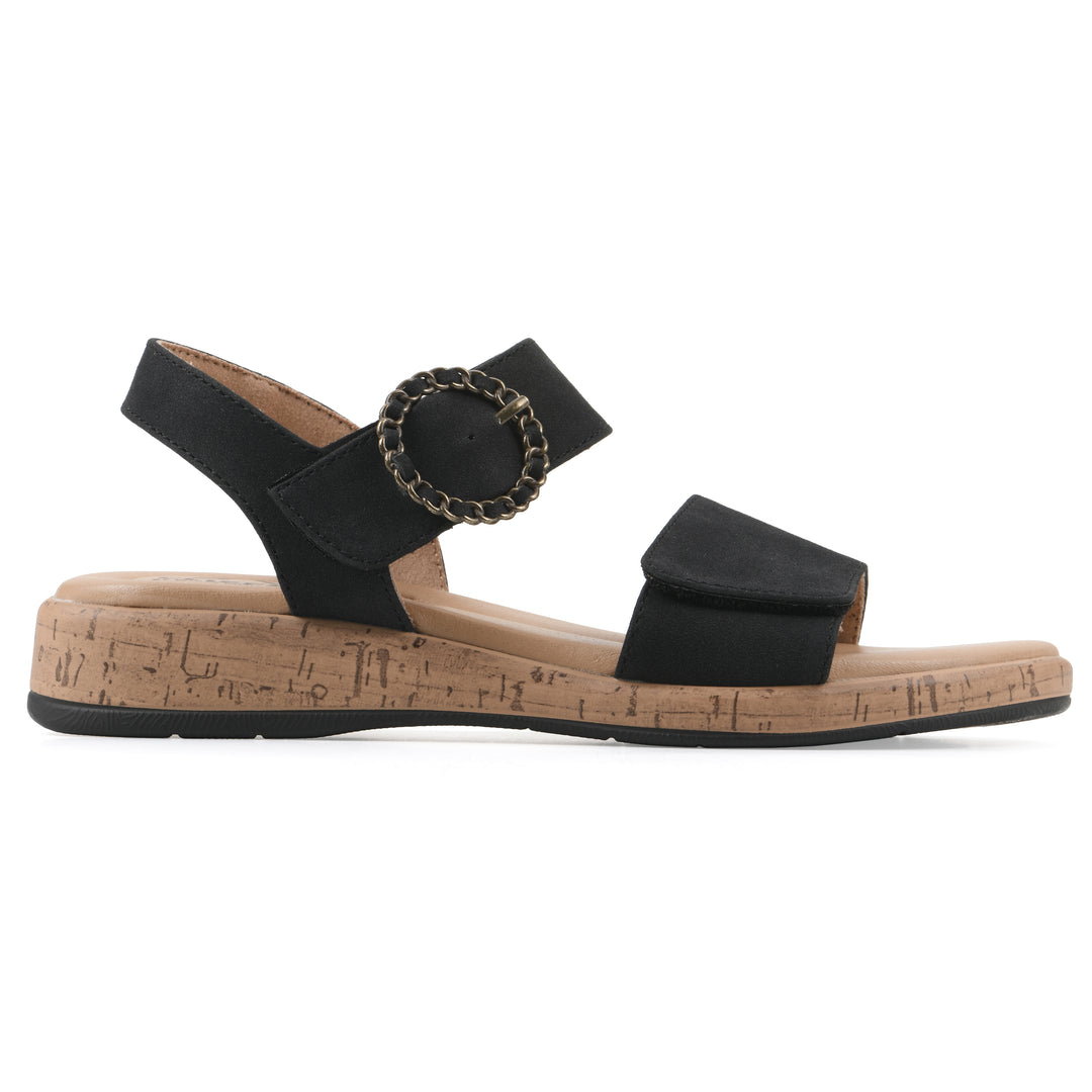 Side view of a black sandal with double adjustable straps, circular buckle embellishment, and low cork print wedge 