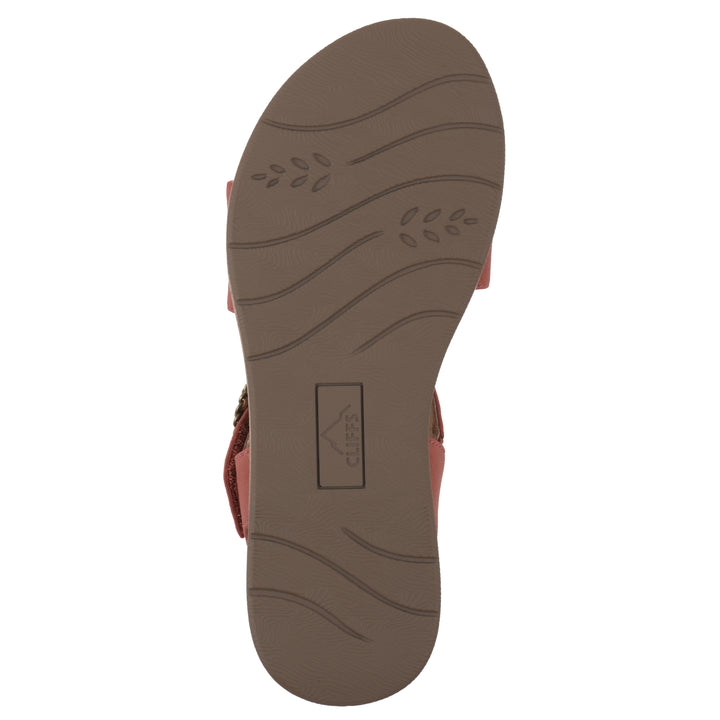 Sole view of a dusty orange sandal with double adjustable straps, circular buckle embellishment, and low cork print wedge 
