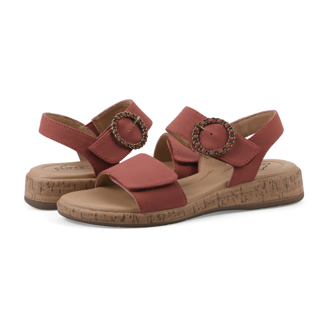 Angle view of a pair of dusty orange sandals with double adjustable straps, circular buckle embellishment, and low cork print wedge 