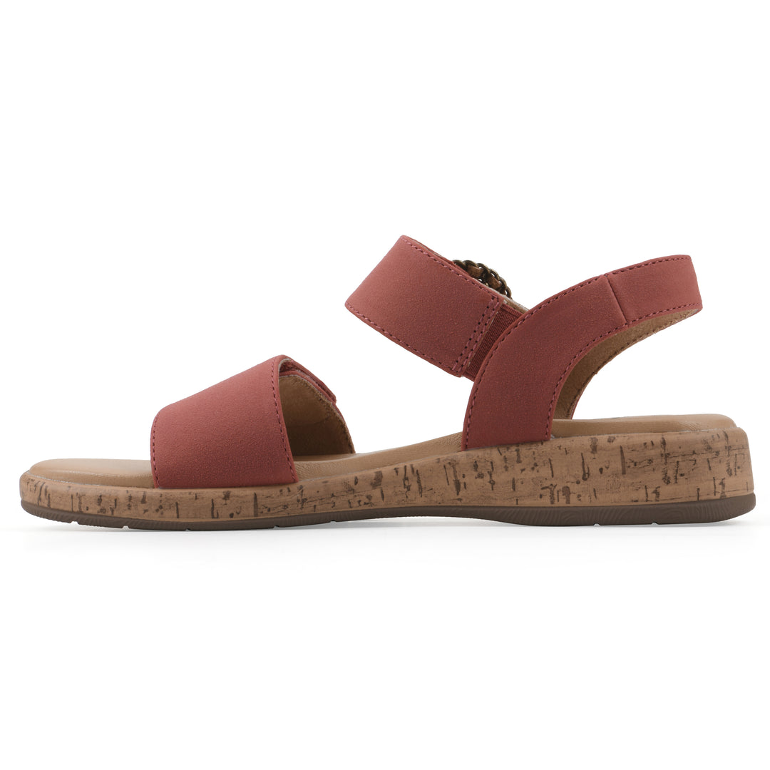 Side view of a dusty orange sandal with double adjustable straps, circular buckle embellishment, and low cork print wedge 