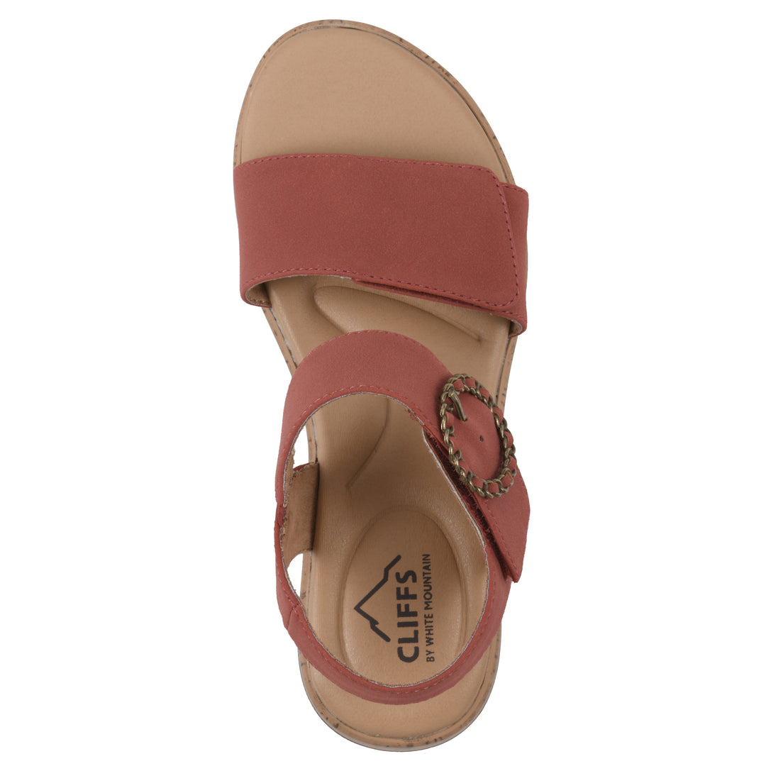 Top view of a dusty orange sandal with double adjustable straps, circular buckle embellishment, and low cork print wedge 