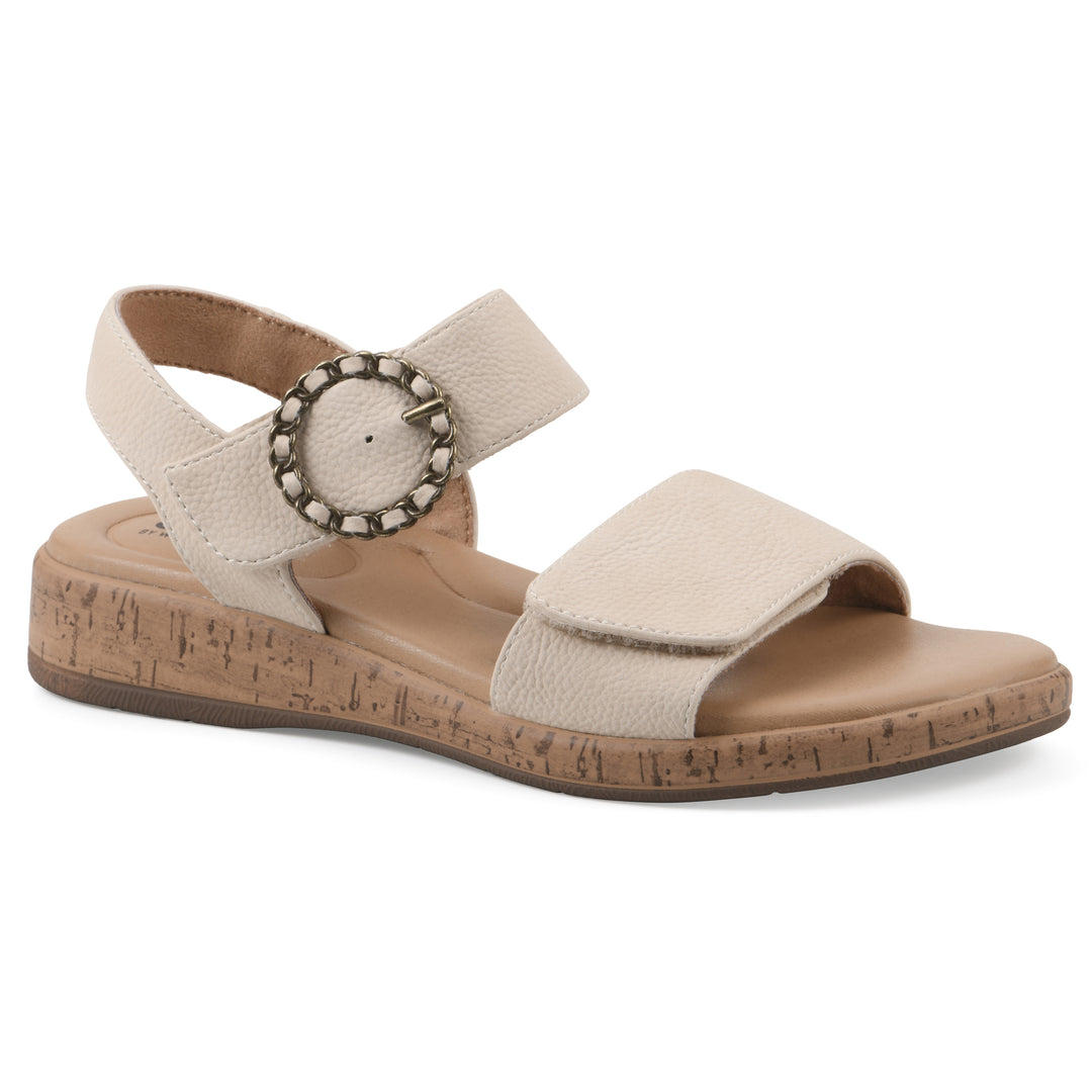 Angle view of a cream sandal with double adjustable straps, circular buckle embellishment, and low cork print wedge 