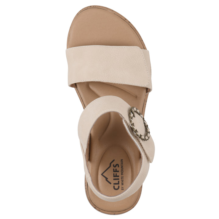 Top view of a cream sandal with double adjustable straps, circular buckle embellishment, and low cork print wedge 