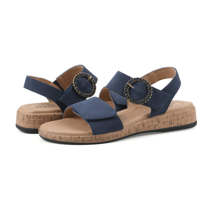 Angle view of a pair of dark blue sandals with double adjustable straps, circular buckle embellishment, and low cork print wedge 
