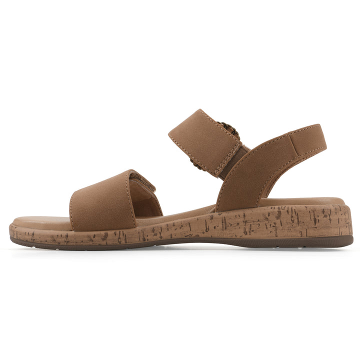 Side view of a tan sandal with double adjustable straps, circular buckle embellishment, and low cork print wedge 