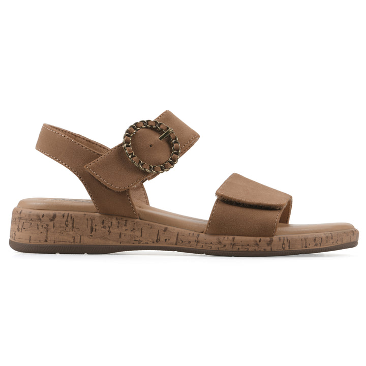 Side view of a tan sandal with double adjustable straps, circular buckle embellishment, and low cork print wedge 