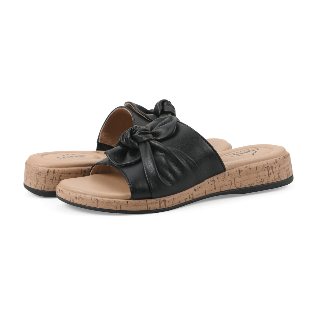Angle view of a pair of black faux leather sandals with centered twist, and cork-print sole design