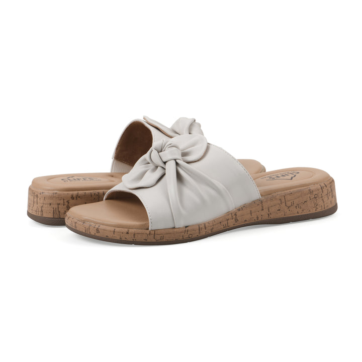 Angle view of a pair of white faux leather sandals with centered twist, and cork-print sole design