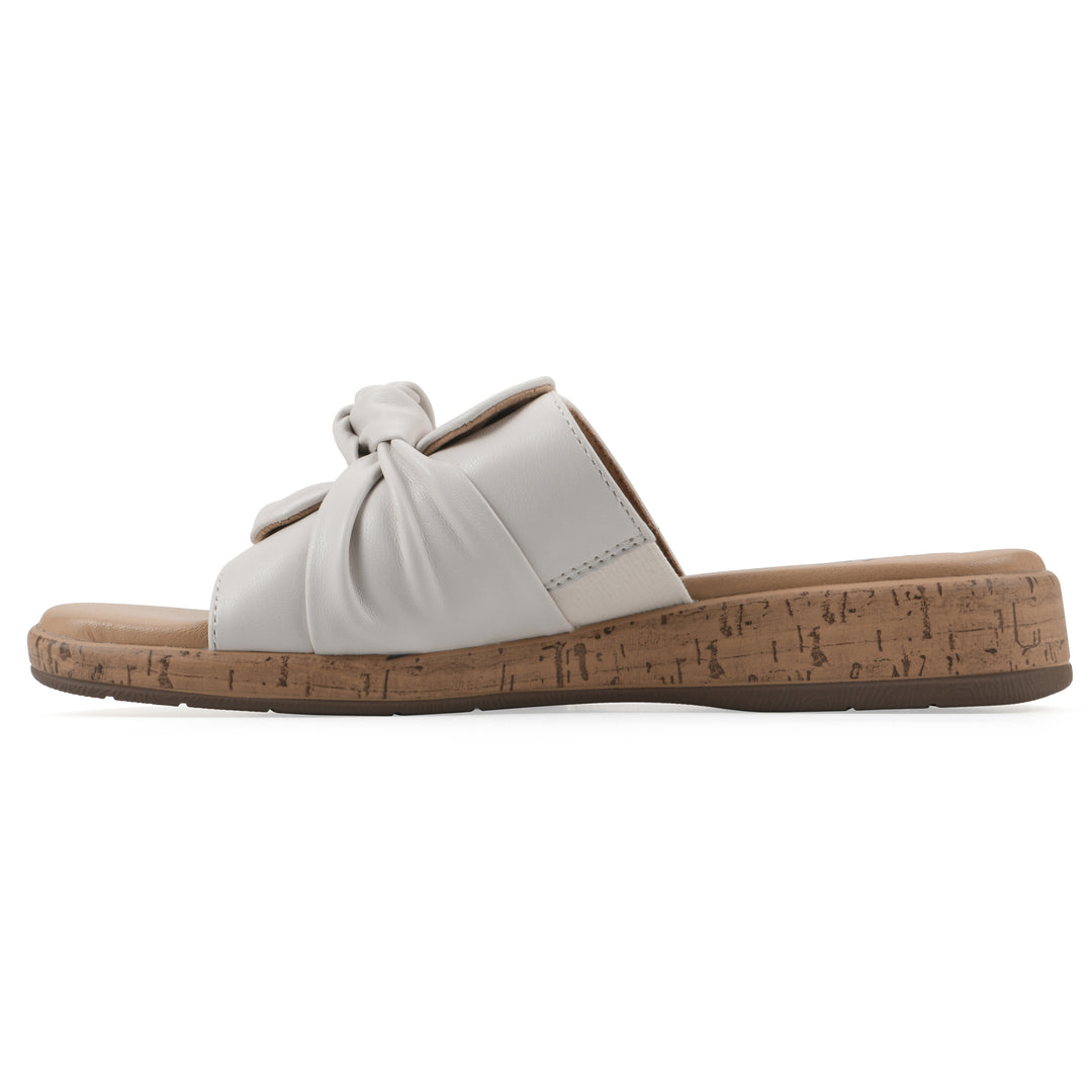 Side view of a white faux leather sandal with centered twist, and cork-print sole design