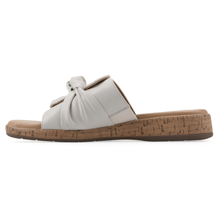 Side view of a white faux leather sandal with centered twist, and cork-print sole design