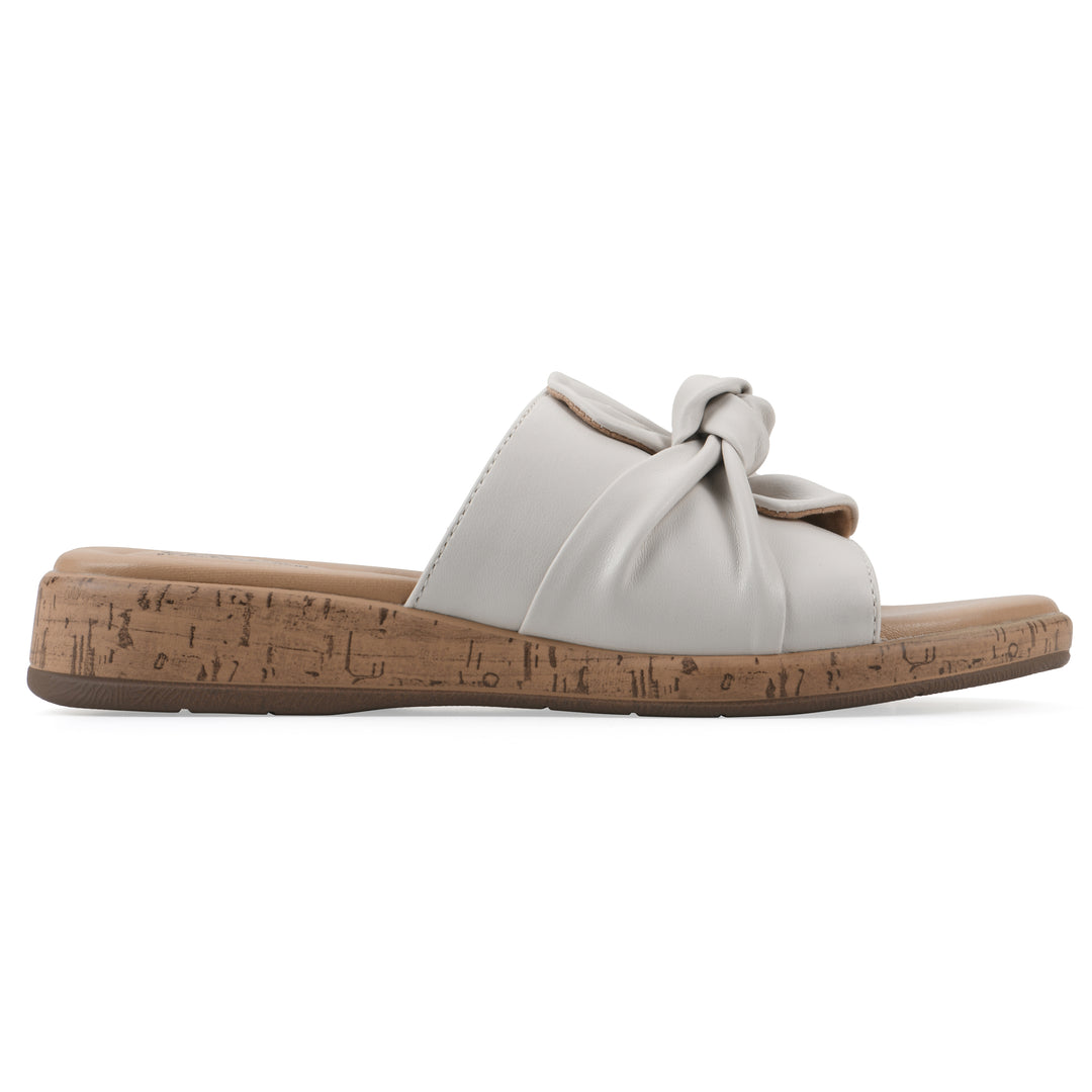 Side view of a white faux leather sandal with centered twist, and cork-print sole design