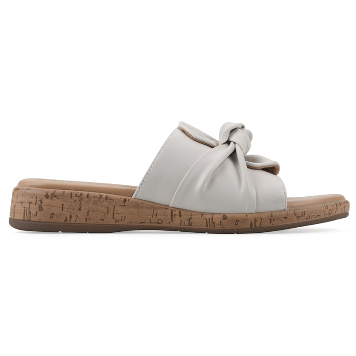Side view of a white faux leather sandal with centered twist, and cork-print sole design