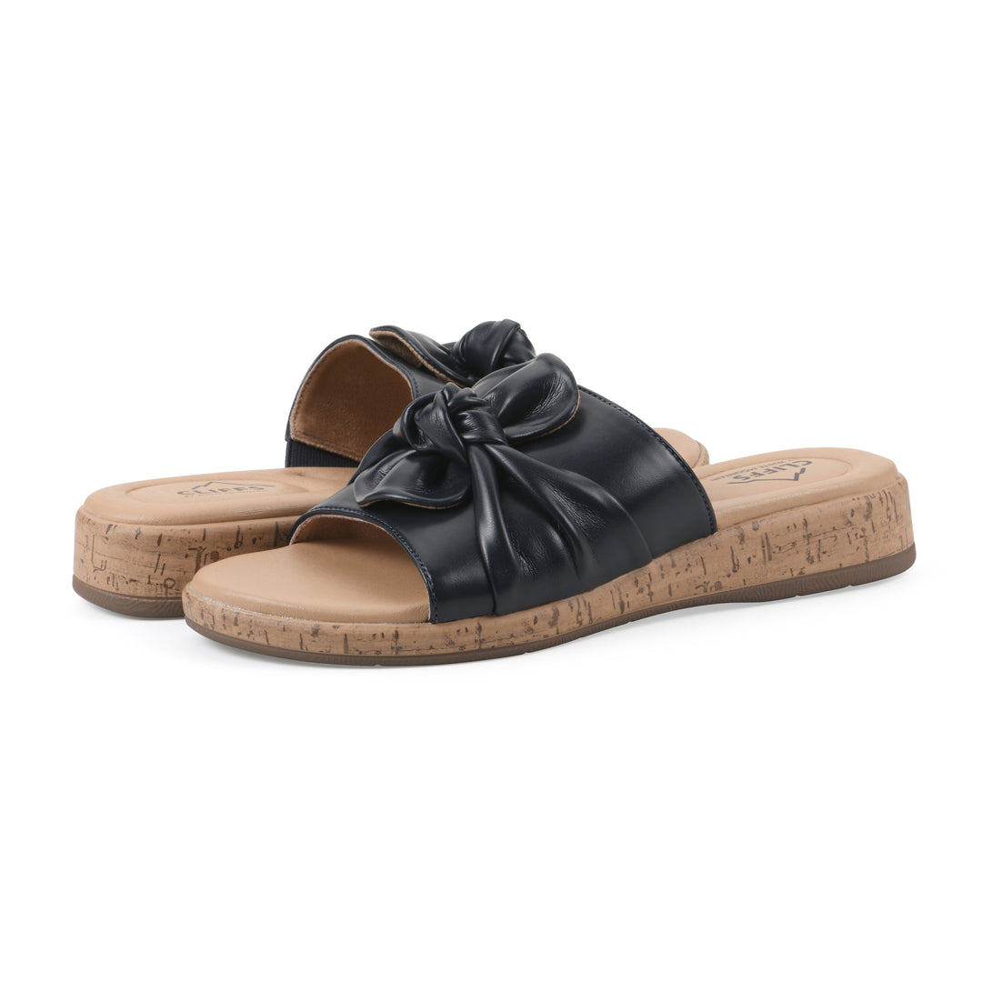 Angle view of a pair of black faux leather sandals with centered twist, and cork-print sole design
