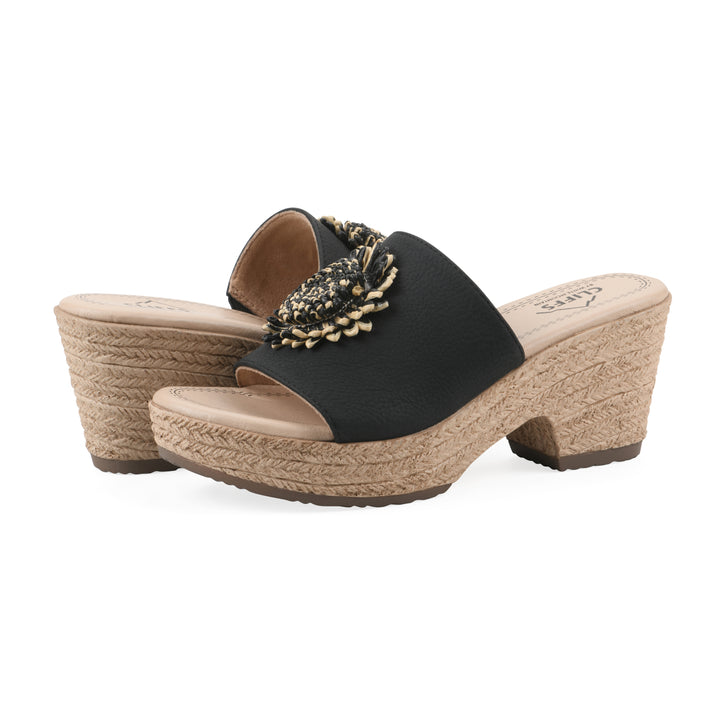 Angle view of a pair of black, backless wedge sandals with centered sunflower embellishment, and braided rope style heel