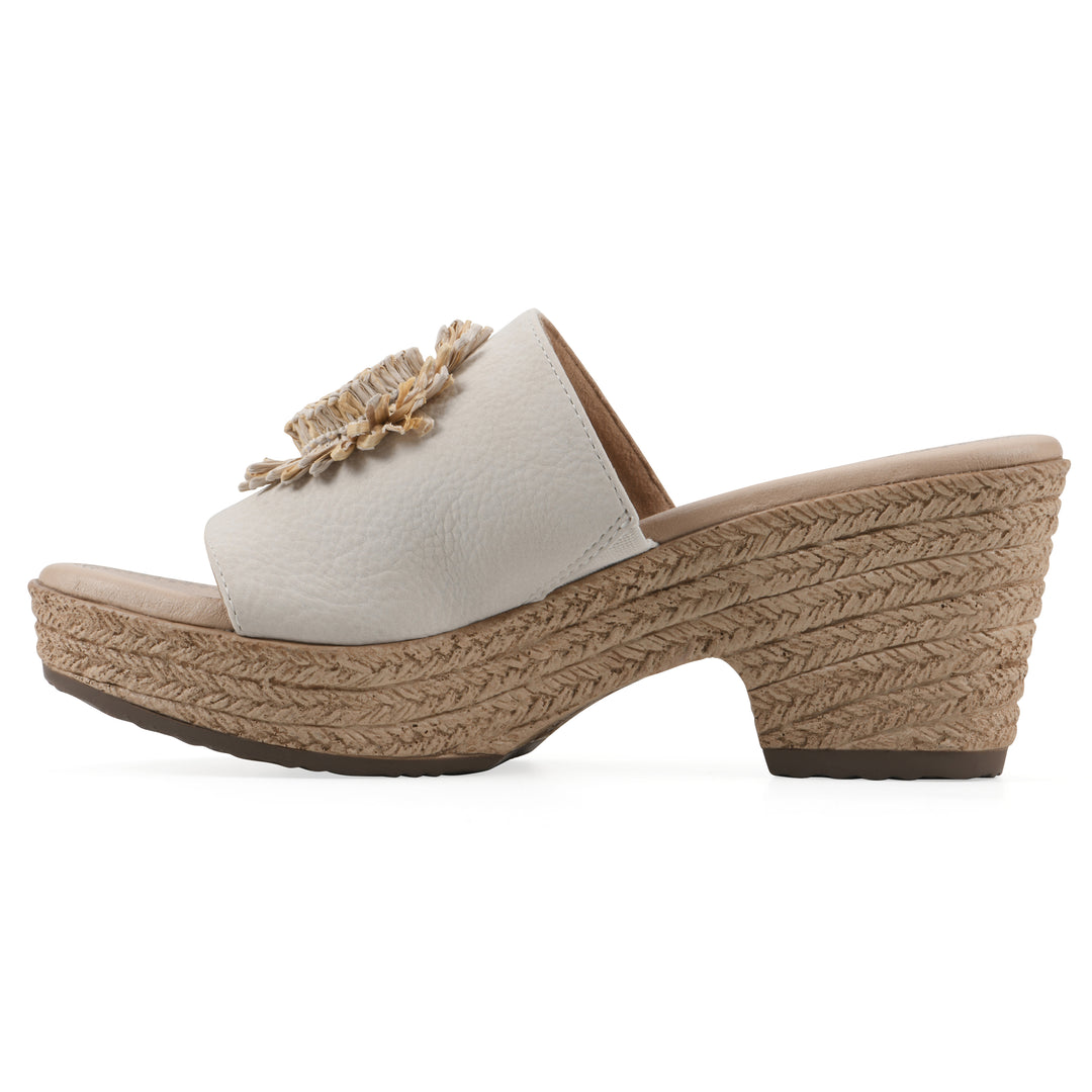 Side view of a cream, backless wedge sandal with centered sunflower embellishment, and braided rope style heel