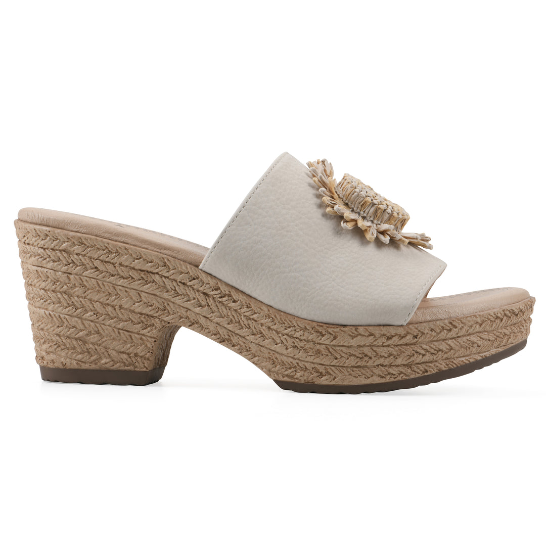 Side view of a cream, backless wedge sandal with centered sunflower embellishment, and braided rope style heel
