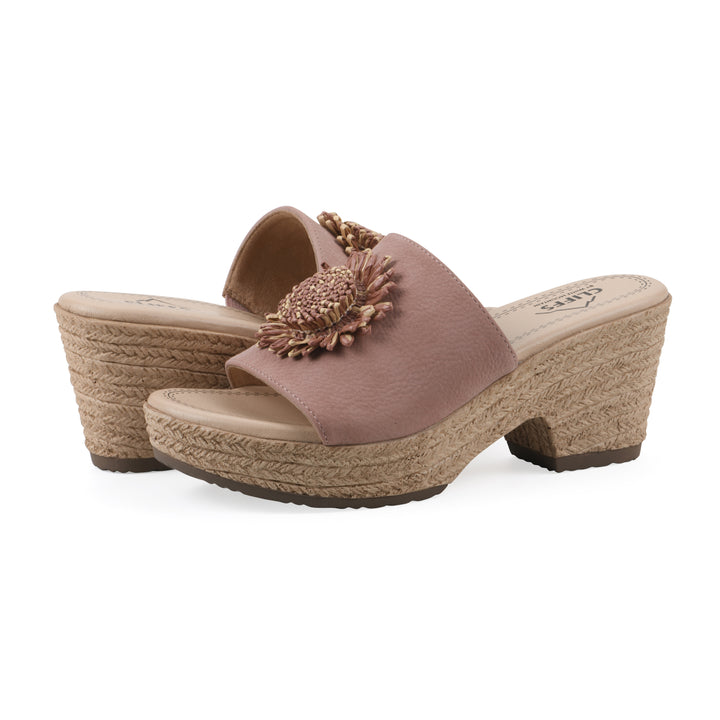 Angle view of a pair of taupe, backless wedge sandals with centered sunflower embellishment, and braided rope style heel