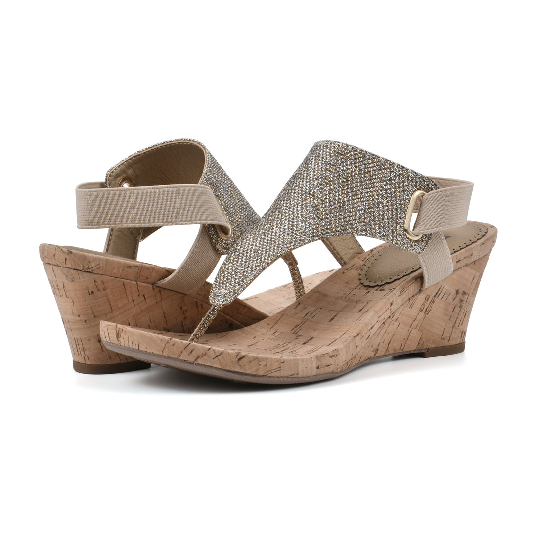 Angle view of a pair of light gold fabric thong wedge sandals with cork heel, and elastic ankle strap