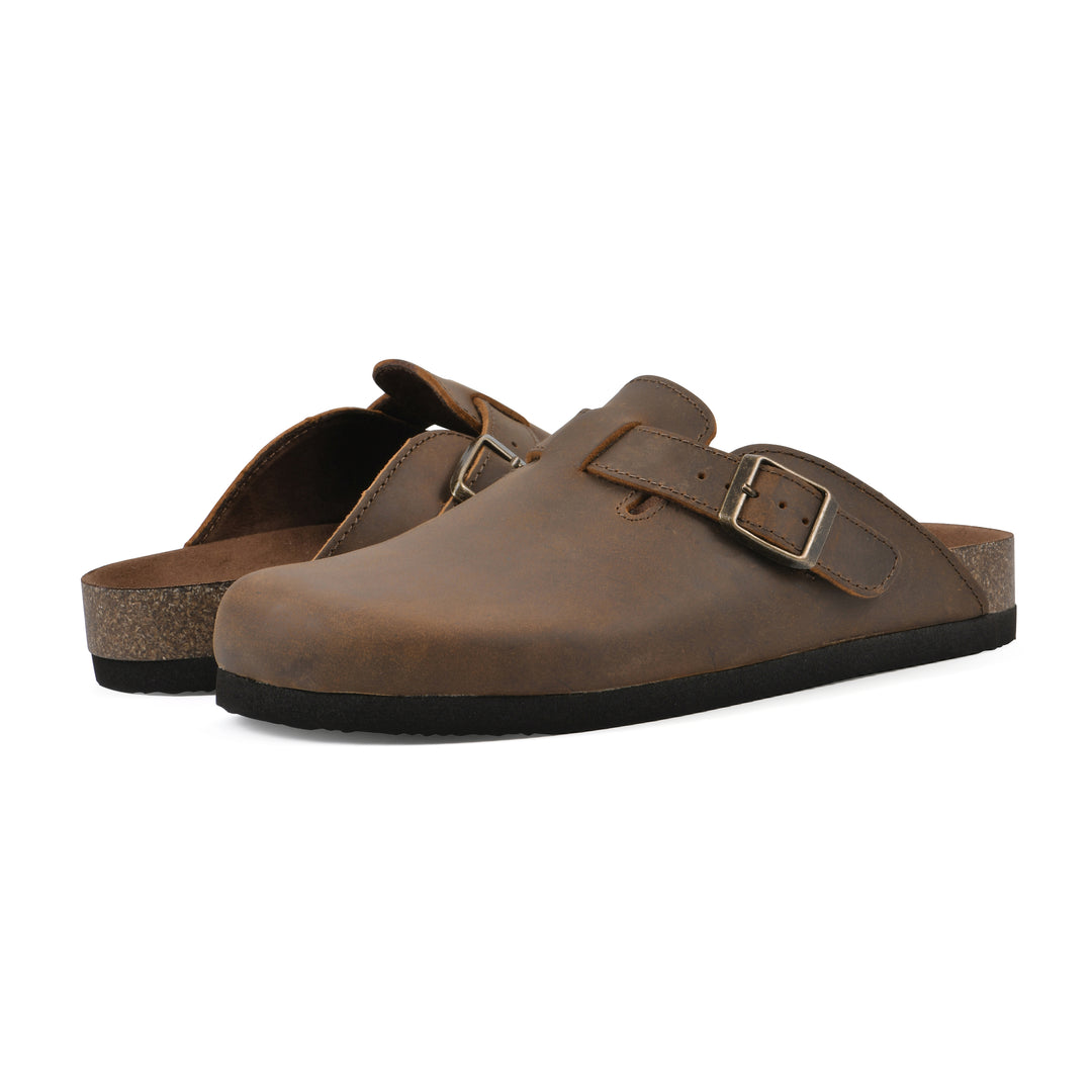 Angle view of a pair of whiskey leather clogs with metal buckle on an adjustable strap, and a brown sole with black bottom