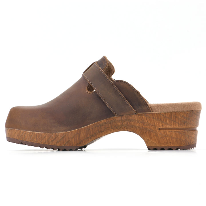 Side view of a backless brown leather clog with adjustable buckle and wood style heel