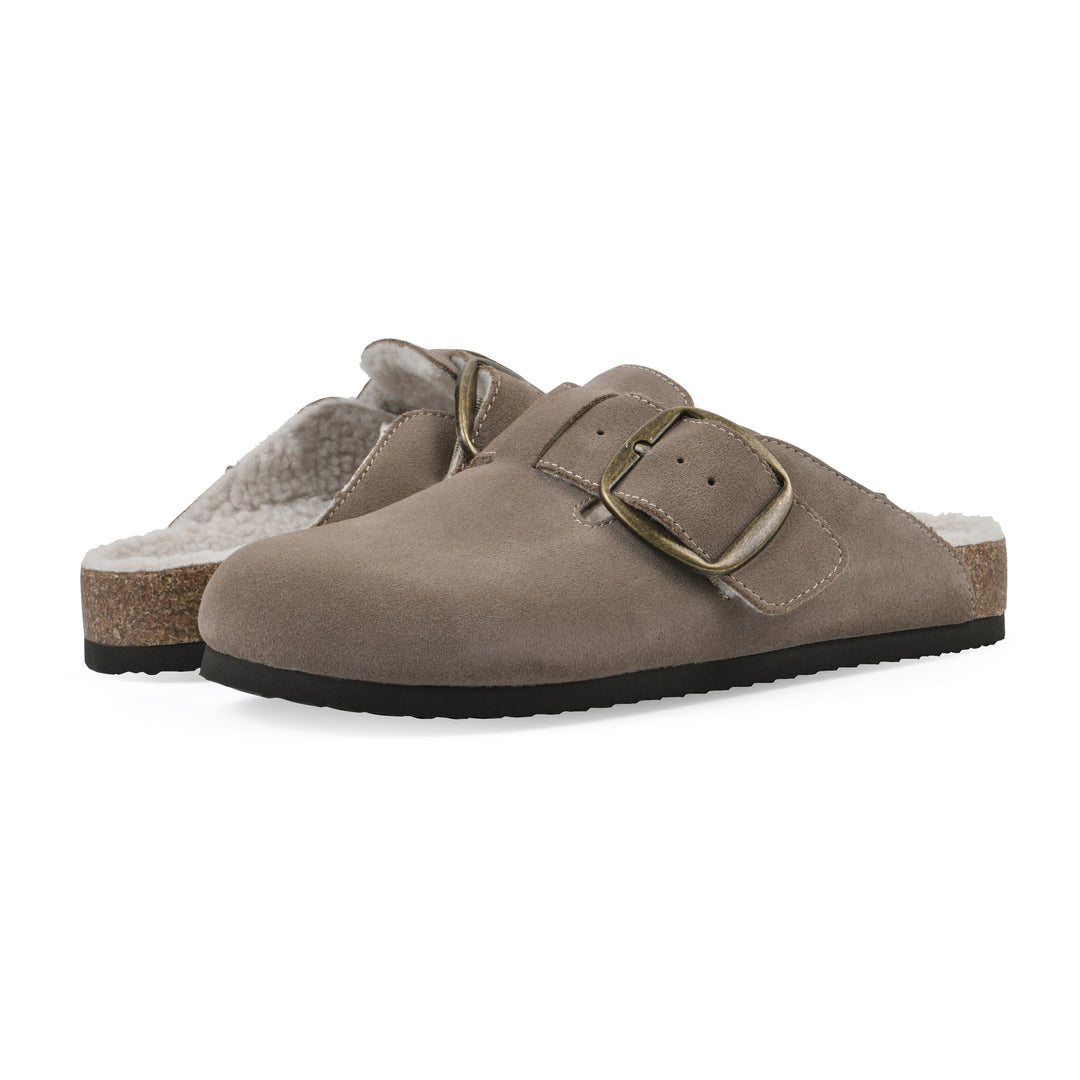 Angle view of a pair of taupe suede backless clogs with cream, faux fur lining, a large adjustable buckle, and a black sole