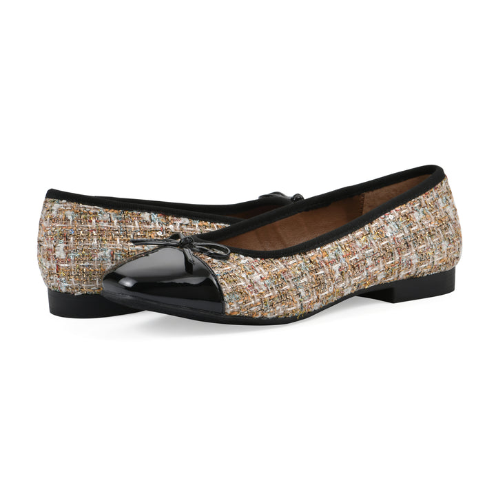 Angle view of a pair of beige boucle fabric flats with small, centered black bow, a smooth black patent toe cap, and a black sole