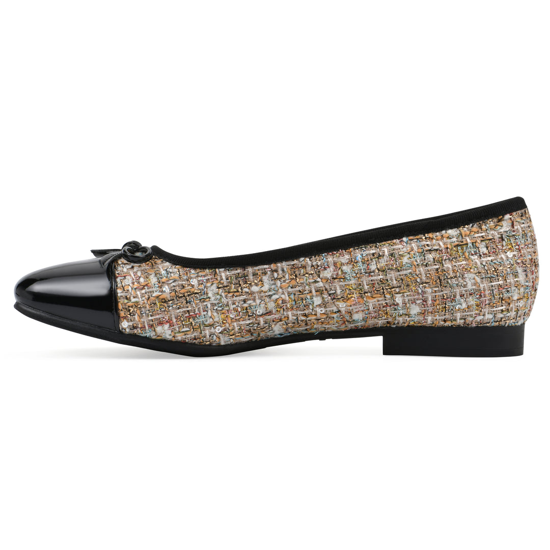 Side view of a beige boucle fabric flat with small, centered black bow, a smooth black patent toe cap, and a black sole
