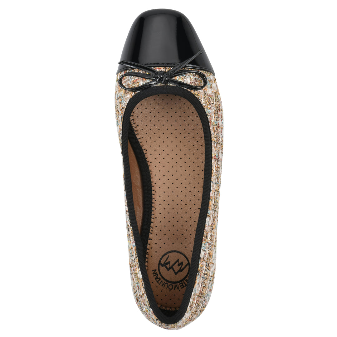 Top view of a beige boucle fabric flat with small, centered black bow, a smooth black patent toe cap, and a black sole