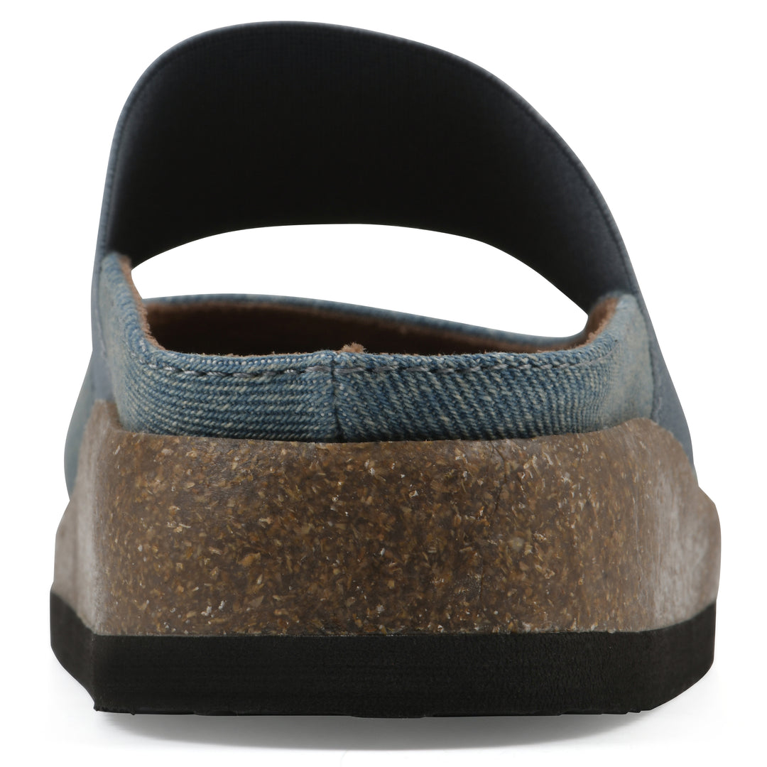 Rear view of a denim backless clog with Mary Jane style center strap and a brown sole with black bottom