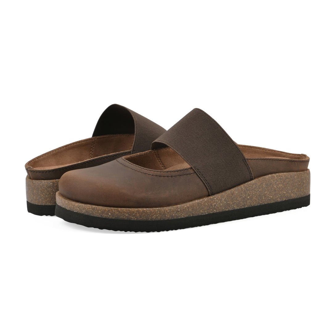 Angle view of a pair of brown leather backless clogs with Mary Jane style center strap and a brown sole with black bottom