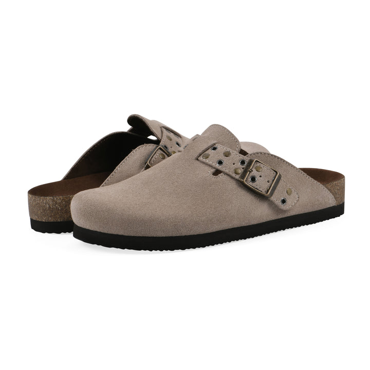 Angle view of a pair of taupe suede backless clogs with an adjustable buckle strap with stud and eyelet detailing and a black sole