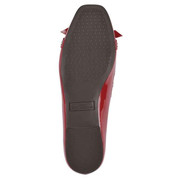 Sole view of a red patent flat with small, centered bow, silver metal grommet lining and a black sole