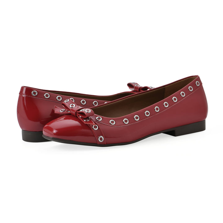 Angle view of a pair of red patent flats with small, centered bow, silver metal grommet lining and a black sole