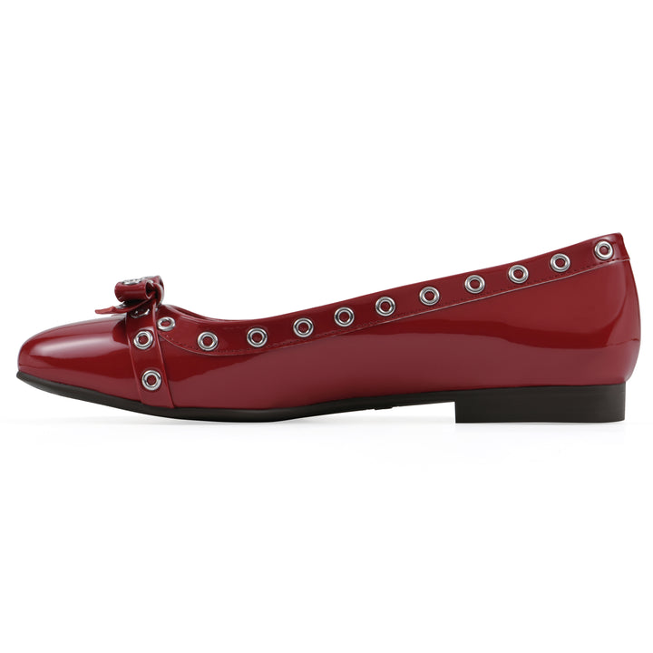 Side view of a red patent flat with small, centered bow, silver metal grommet lining and a black sole