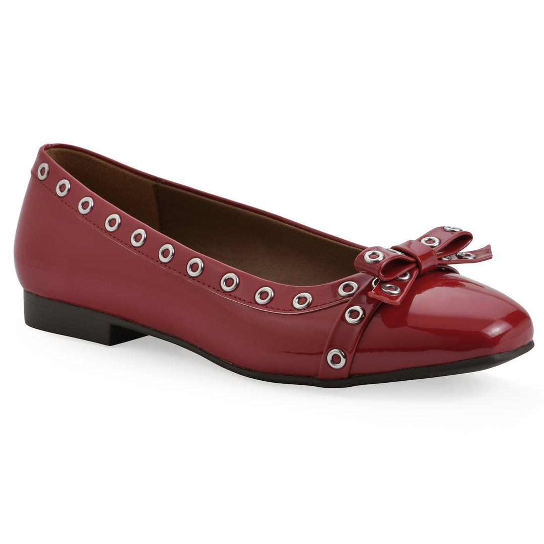 Angle view of a red patent flat with small, centered bow, silver metal grommet lining and a black sole