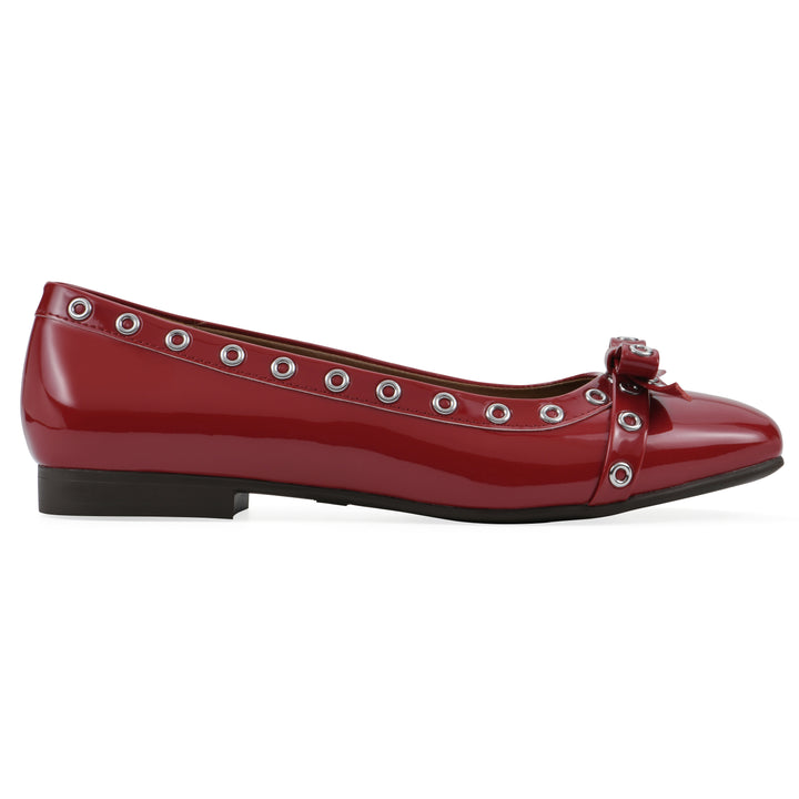Side view of a red patent flat with small, centered bow, silver metal grommet lining and a black sole