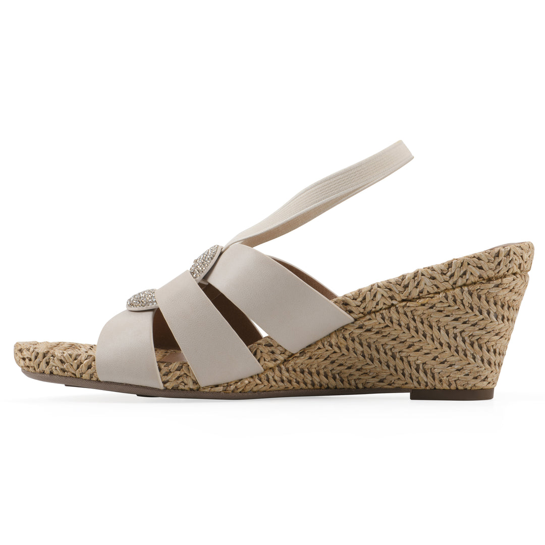 Side view of a cream wedge sandal with elastic heel strap, woven raffia sole and a centered, sequin applique