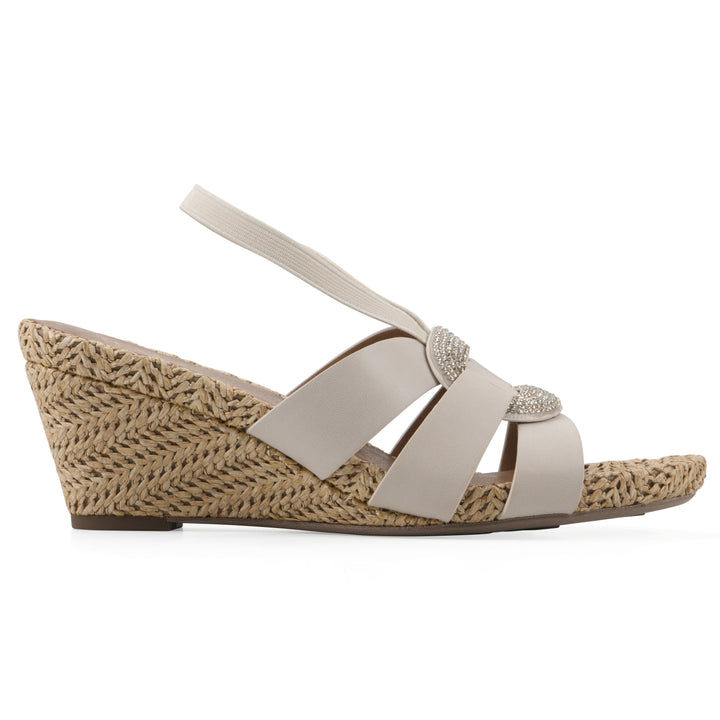 Side view of a cream wedge sandal with elastic heel strap, woven raffia sole and a centered, sequin applique