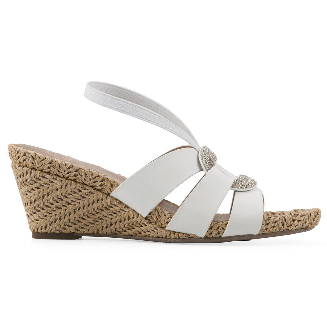 Side view of a white wedge sandal with elastic heel strap, woven raffia sole and a centered, sequin applique