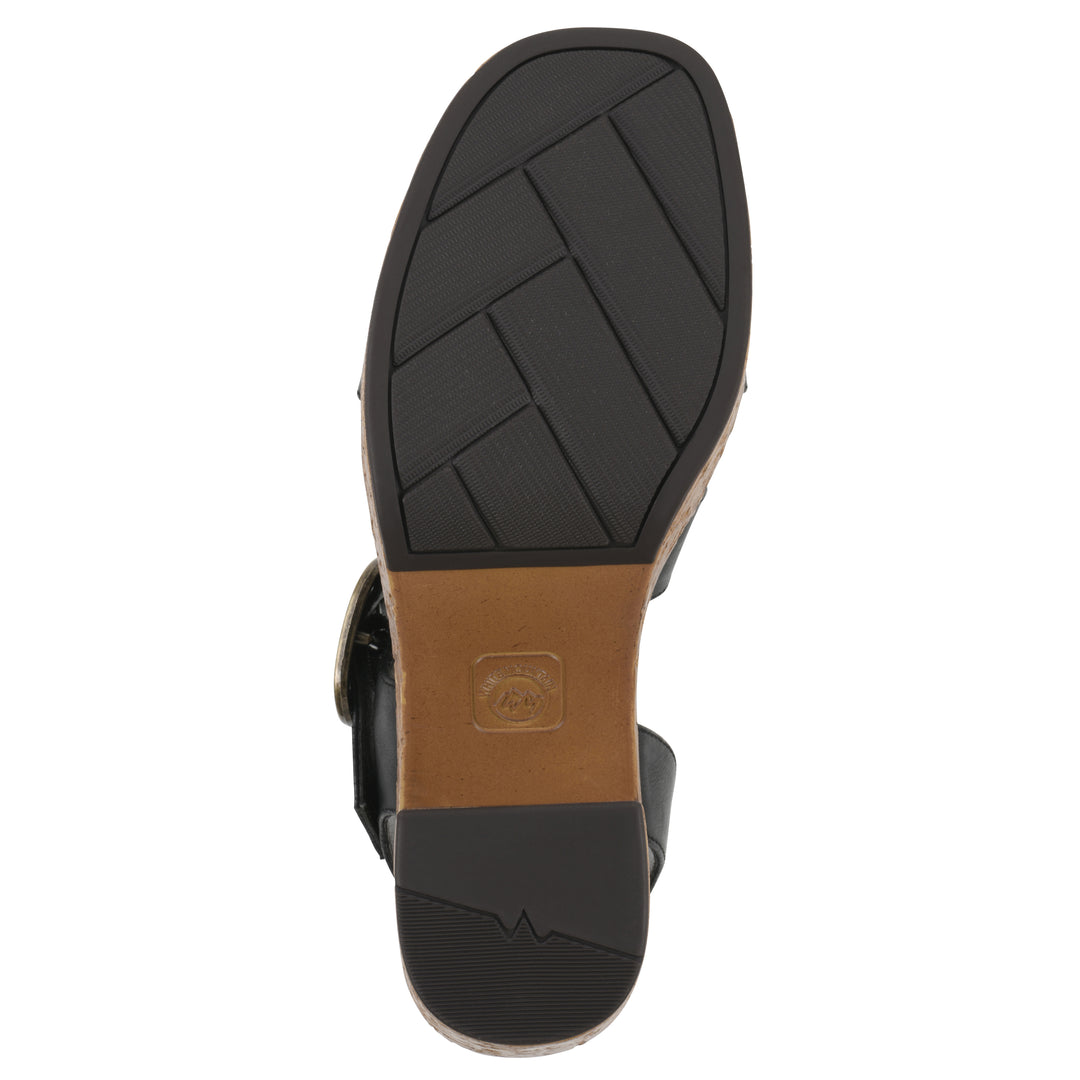 Sole view of a black platform sandal with ankle buckle, a brown, faux cork sole, and black patterned outsole bottom