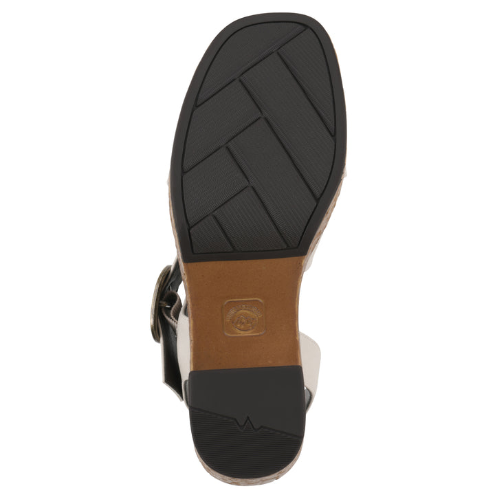 Sole view of a white platform sandal with ankle buckle, a brown, faux cork sole, and black, patterned sole bottom